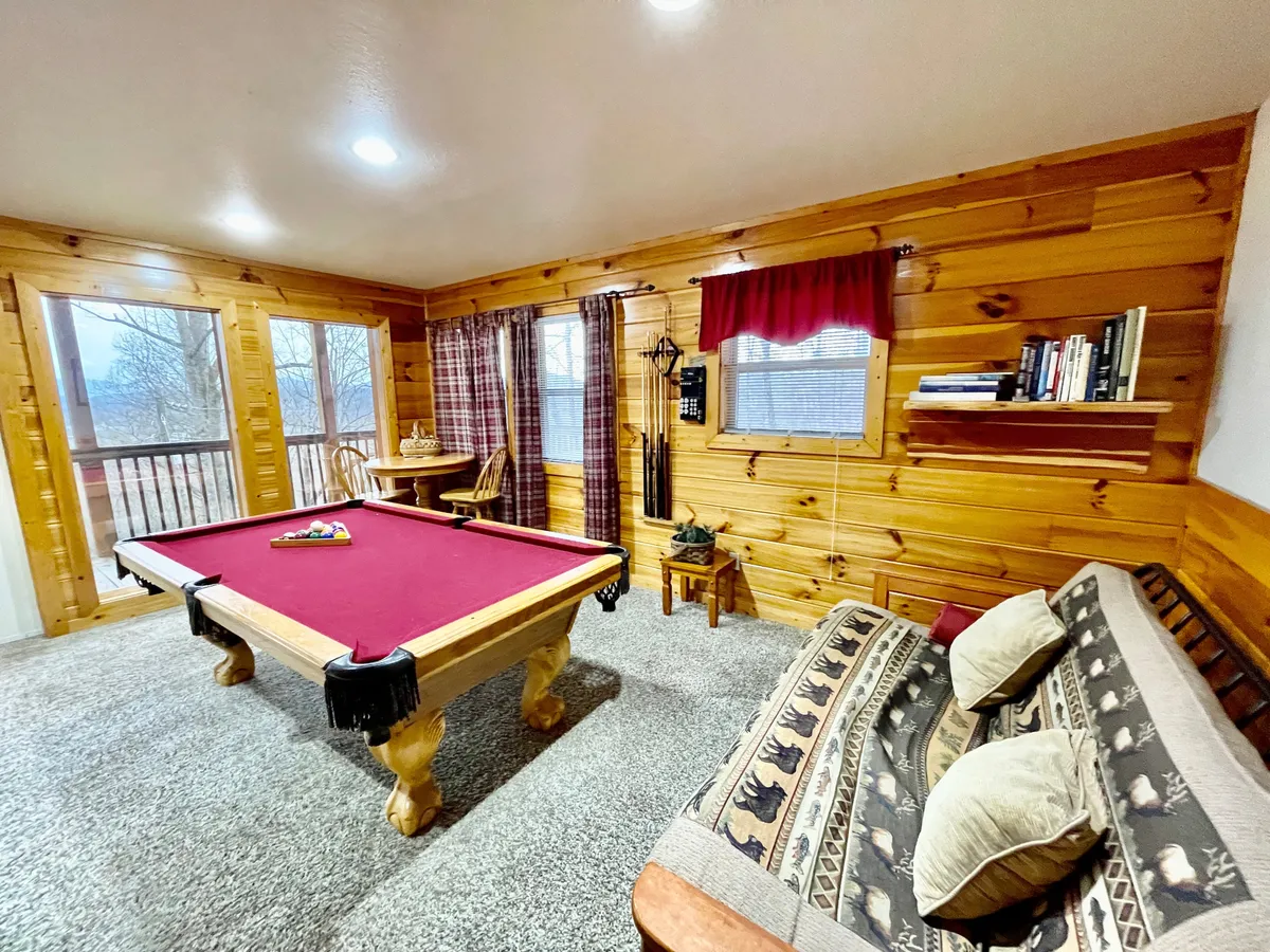 A casual, friendly game room scene with a pool table, cozy sofa, and wide windows. The room feels intimate and relaxed, inviting guests to lounge, play, or gather for conversation. The natural light and comfortable setup evoke the sleepover vibe mentioned in the text.
