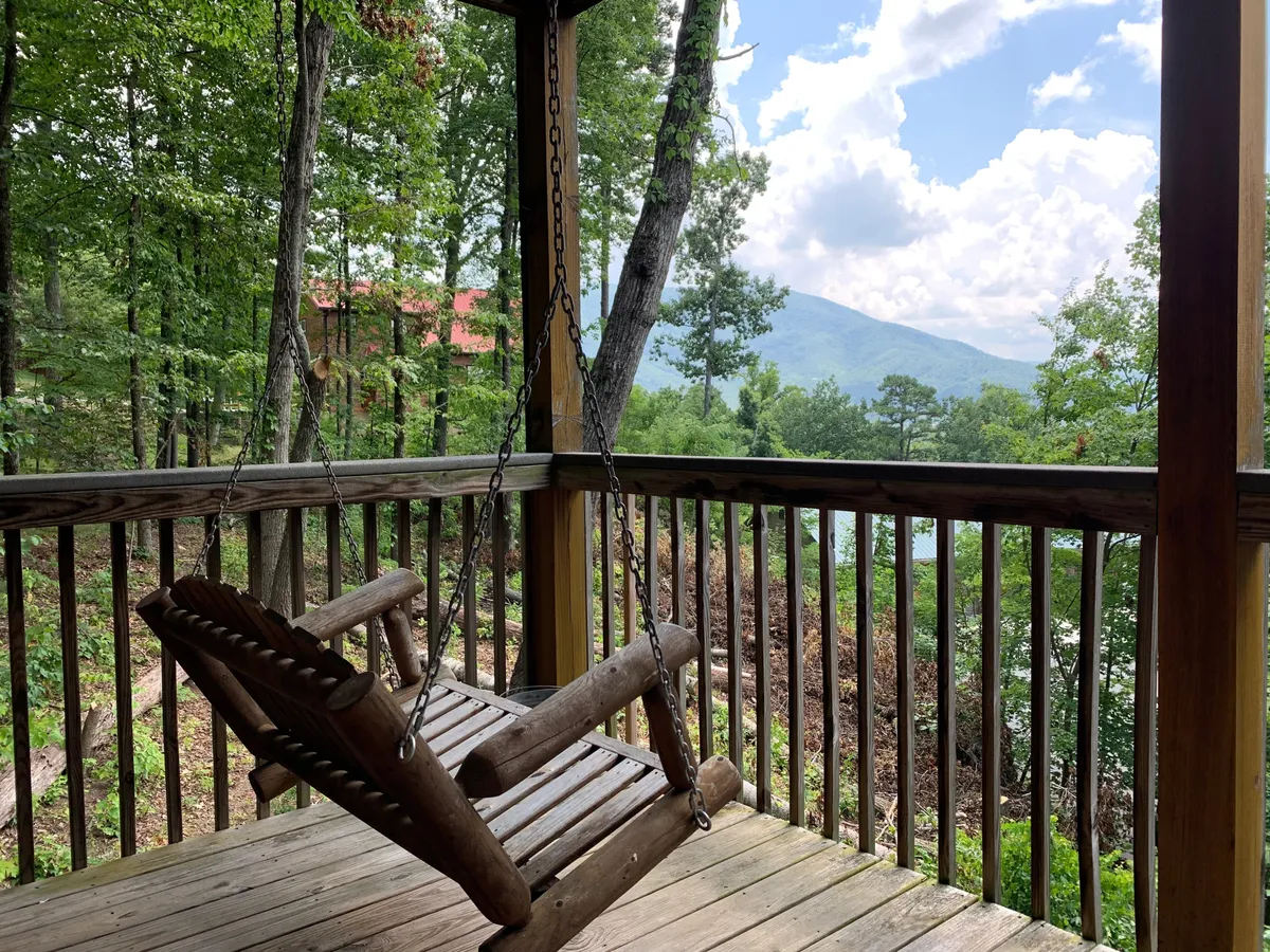 This image shows a wooden swing set on a deck, overlooking stunning mountain views and surrounded by lush green foliage. The atmosphere is peaceful and intimate, with soft natural lighting suggesting either early morning or late afternoon.