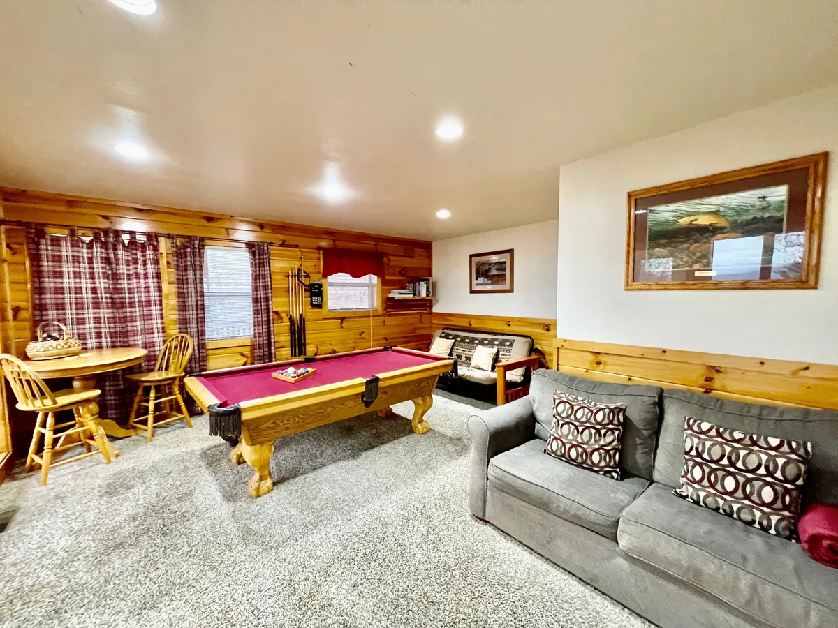An inviting game room featuring a pool table, dining table, and sofa, with soft natural light from curtained windows. The space is set up for family fun, group gatherings, and friendly competitions.