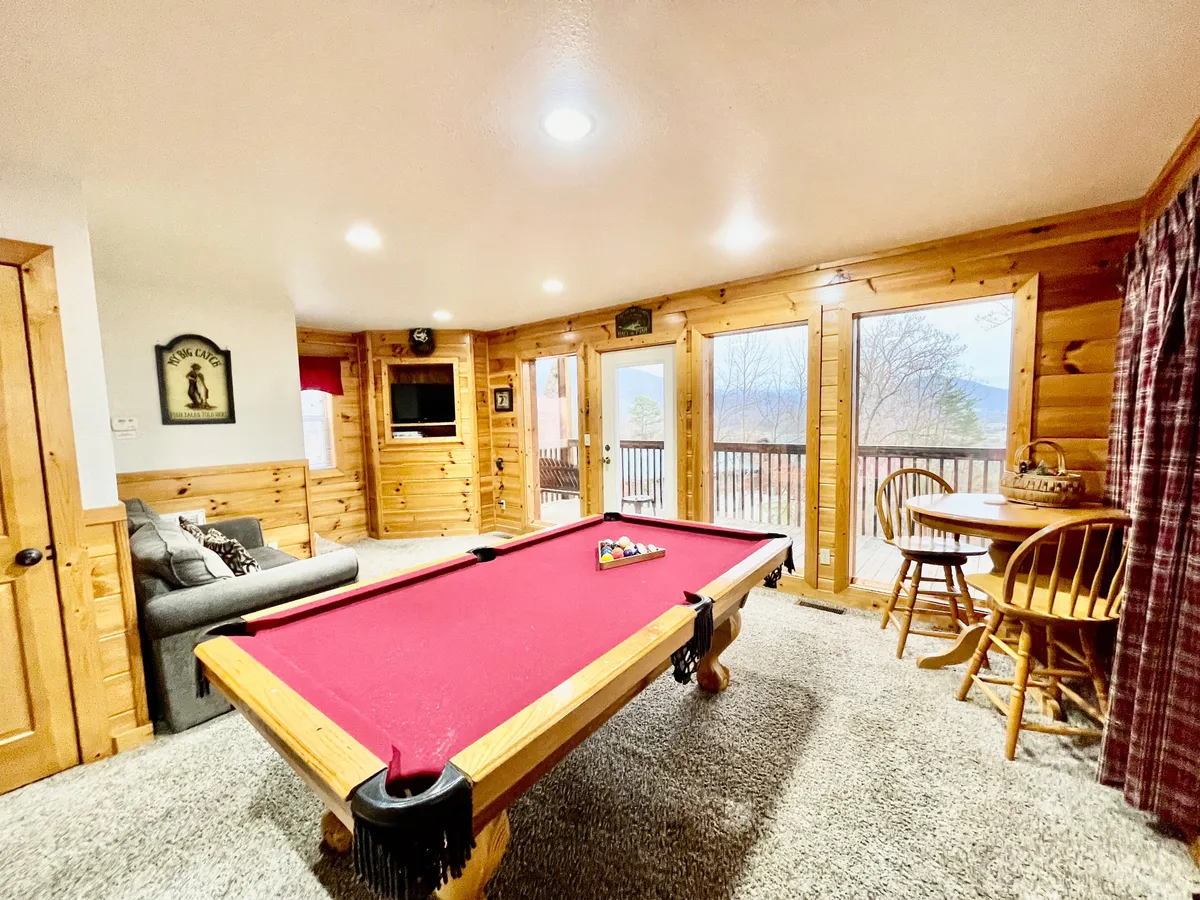 This interior scene centers on a well-lit game room featuring a pool table, a comfortable sofa, bar stools, and large windows letting in natural light. The inviting layout is perfect for both spirited games and relaxation. The visible windows underscore the bright, cheery atmosphere described in the section.