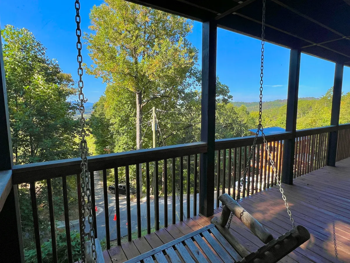 A swing seat nestled in lush greenery with distant rolling hills visible in the background. The setting is peaceful and slightly secluded, perfect for contemplative moments or sharing a quiet morning together.