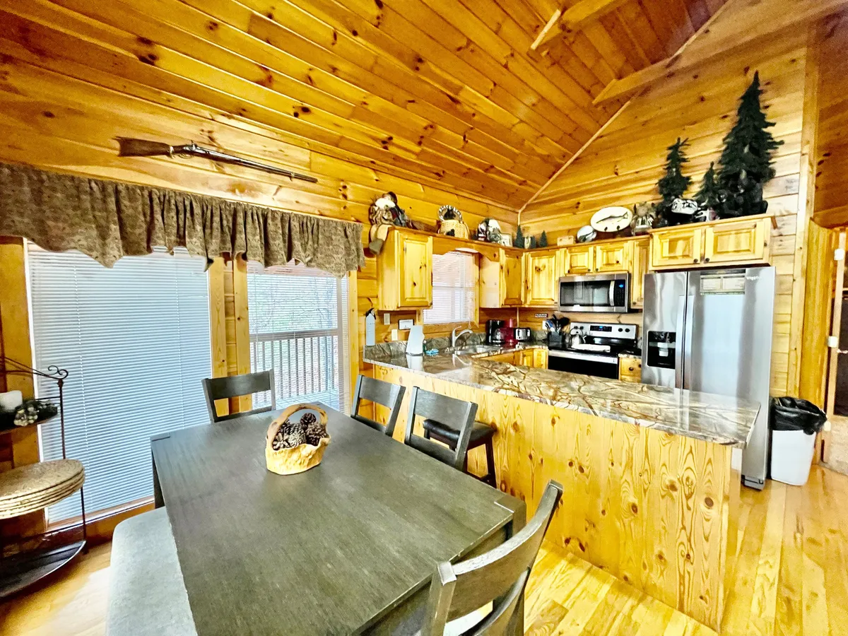 This interior shot centers on a wooden dining table set beside a kitchen island and wooden cabinets, with decorative items on the shelves. The layout encourages conversation and communal activities, echoing the idea of coming together for meals or special occasions.