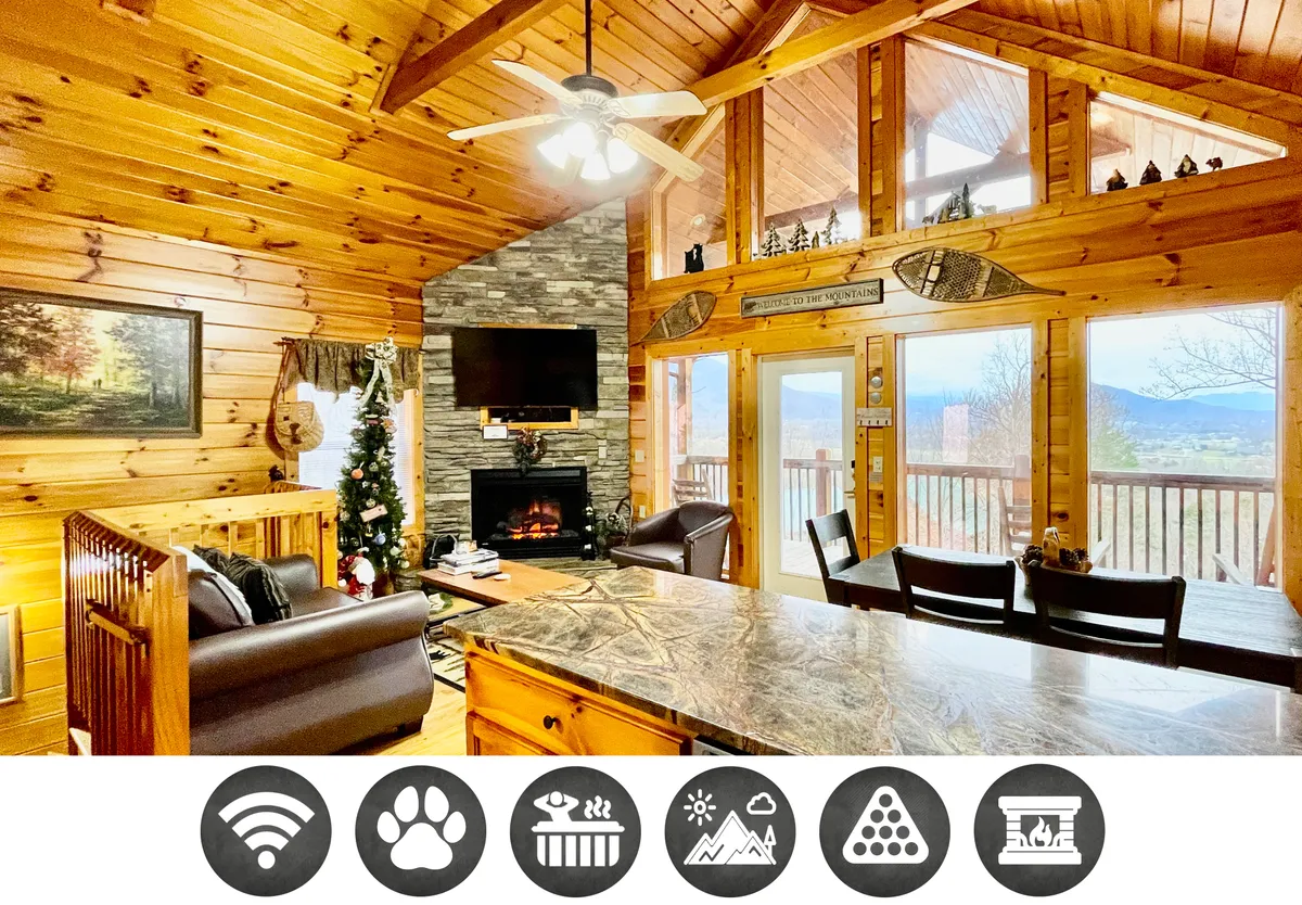 The image showcases a spacious, inviting interior with rustic wooden beams, a striking stone fireplace as the centerpiece, a well-equipped kitchen with a large island, and expansive windows that frame breathtaking mountain views. The setup exudes warmth and offers ample space for guests to gather, relax, and enjoy the scenery.