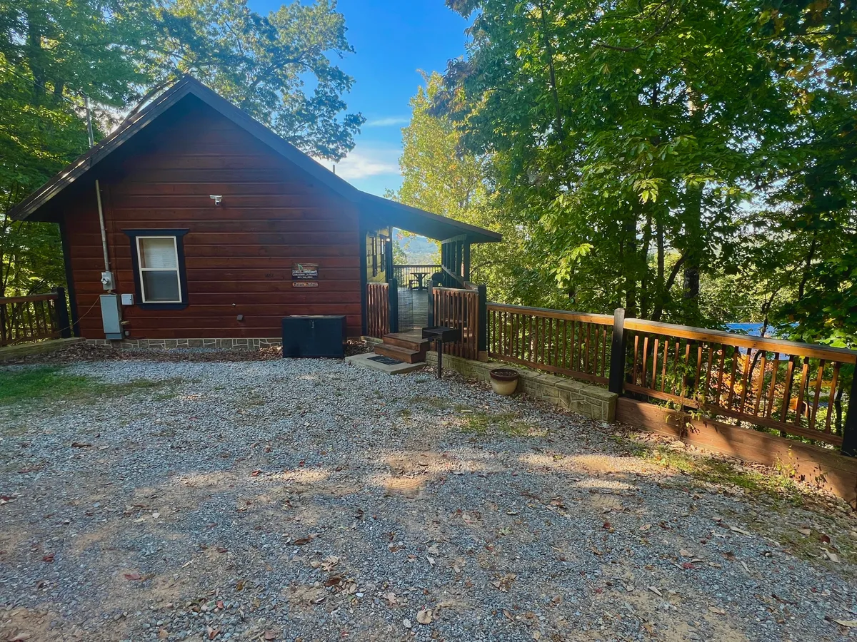 This image shows the rustic wooden cabin set amid lush trees, with a gravel driveway and a spacious deck area. The deck offers a clear connection to the outdoors, and the surrounding greenery suggests ample space for walks and outdoor activities with pets. The tranquil atmosphere reflects the peaceful, nature-immersed experience described in the section.