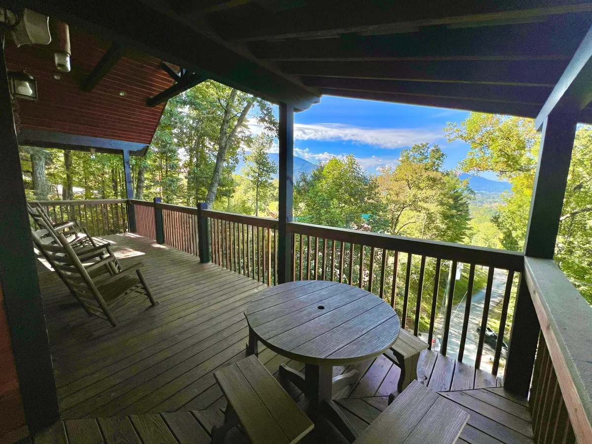 This image features a wooden deck with rocking chairs and a circular table overlooking mountains and trees. The setup is ideal for enjoying scenic views with your pet by your side, while the inviting deck encourages relaxation after a day of hiking or exploring the Smoky Mountains.