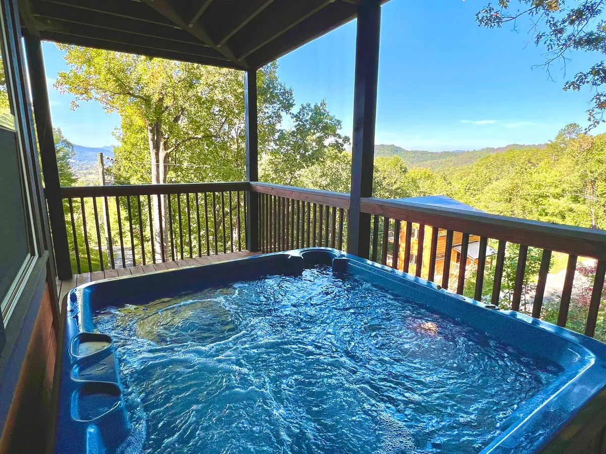 An outdoor hot tub positioned on a deck with a scenic mountain view, surrounded by tranquil nature. The setting is perfect for unwinding under the stars after a day of adventure, with ample space for relaxing and stargazing.