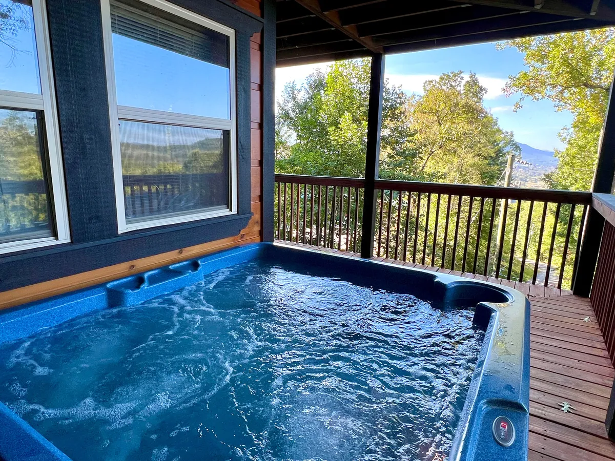 The image features a bubbling hot tub on a wooden deck overlooking trees, perfectly situated for soaking while enjoying mountain views. The scene is tranquil yet hints at post-adventure relaxation surrounded by natural beauty.
