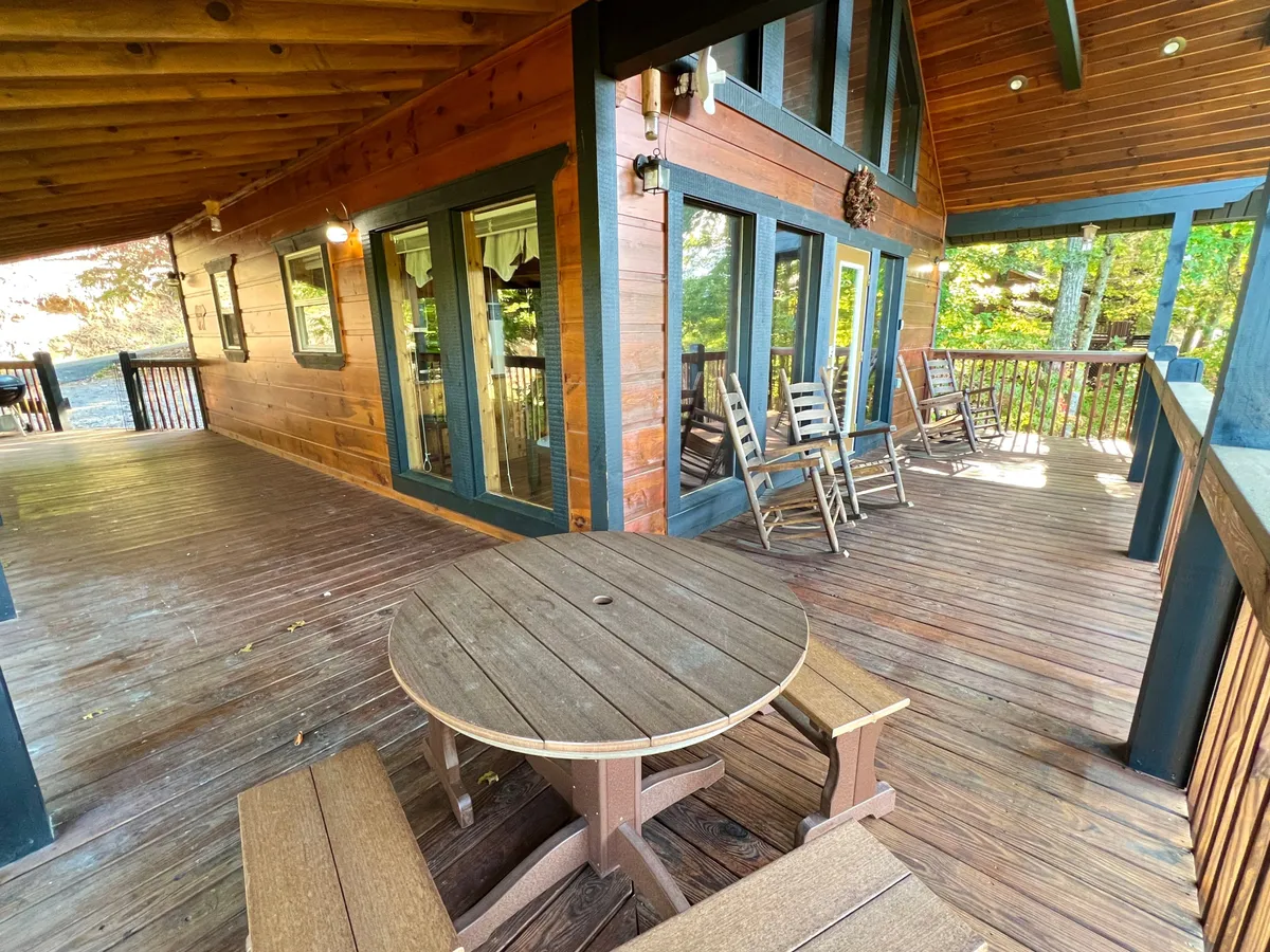 A comfortable section of the wooden deck with a table, rocking chairs, and large windows that seamlessly blend the indoors with the outdoors. The seating arrangement invites conversation and relaxation, set against the backdrop of peaceful natural views.